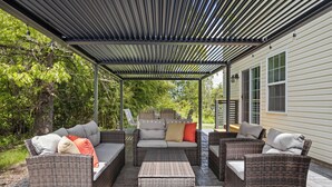A covered patio area with wicker furniture, including sofas and a coffee table, and a pergola overhead.
