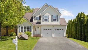 Une maison à deux étages avec une allée menant à l’entrée, une boîte aux lettres et un grand rocher dans le jardin.