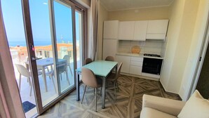 A compact living space with a dining area, kitchenette, and a sliding glass door leading to an outdoor terrace. - Appartamenti Borgo Panoramico N.6 (Tropea)