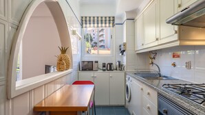 A compact kitchen with a wooden table, a washing machine, a microwave, and a gas stove.