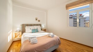 A neatly arranged bedroom with a bed, bedside tables, and a window with a view of buildings.