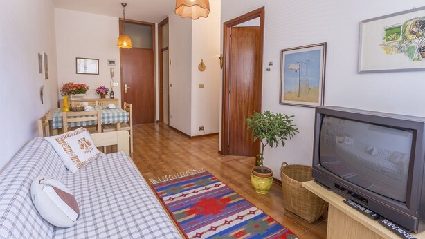 A cozy living room with a sofa, TV, and a dining area with a table and chairs. - Lignano Sea & Relax Apartment (Lignano Sabbiadoro)