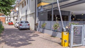 A residential street with parked cars, a gated entrance, and a building with large windows and balconies. - Lignano Sea & Relax Apartment (Lignano Sabbiadoro)