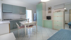 A compact kitchen with teal cabinets, a dining table with chairs, a refrigerator, and a television.
