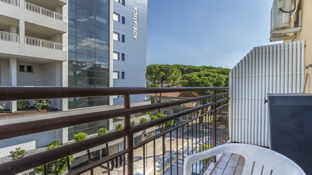 A balcony with a view of a modern building, a parked car, and a clear sky.