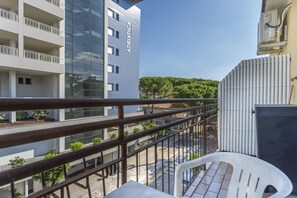 Een balkon met uitzicht op een modern gebouw, een geparkeerde auto en een heldere lucht.