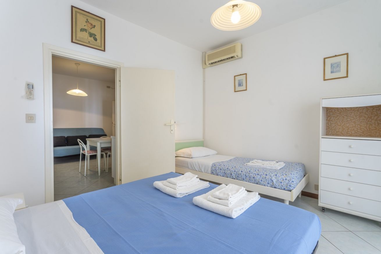 Een slaapkamer met twee bedden, een bureau en een stoel. Er is een deur naar een andere kamer en een airconditioning aan de muur.