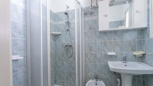 A bathroom with a glass-enclosed shower, a pedestal sink, and a bidet.