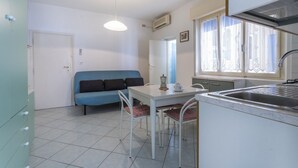 A compact kitchen with a dining table, a blue sofa, and a window with lace curtains.