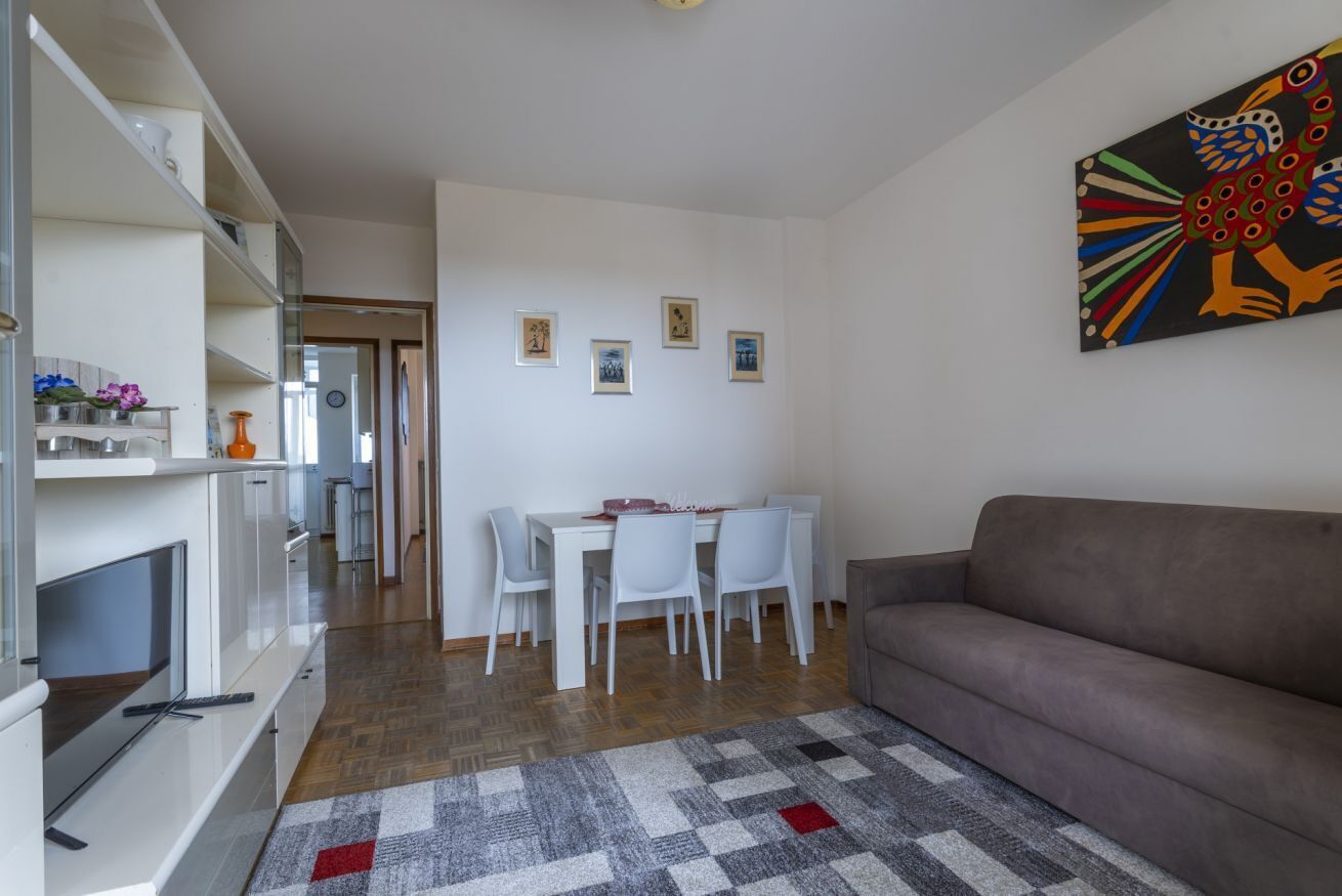 Ein modernes Wohnzimmer mit einer Couch, einem Essbereich mit Tisch und Stühlen sowie einer Küchenzeile mit Schränken und einem Fernseher.