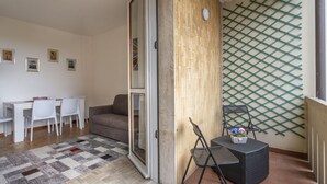 A room with a dining area, a sofa, a small table with chairs, a patterned rug, and a wall-mounted rack. - Zia Dina Apartment (Pasian di Prato)