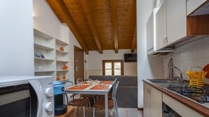 A compact kitchen with a microwave, coffee maker, and stove. There is a dining table with chairs and a bench. - Leisure & Business (Buttrio)