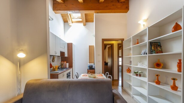 A cozy living area with a sofa, a dining table with chairs, a kitchen in the background, and a bookshelf with decorative items. - Leisure & Business (Buttrio)