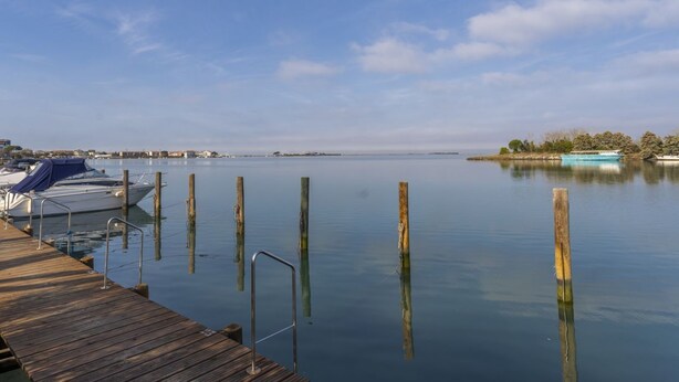 Una orilla tranquila con un muelle de madera, barcos y cielo despejado.
