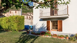 A white building with a balcony, surrounded by a well-maintained garden with potted plants and flowers. - Borgo Santa Lucia Apartment with Private Parking & Garden (Gubbio)