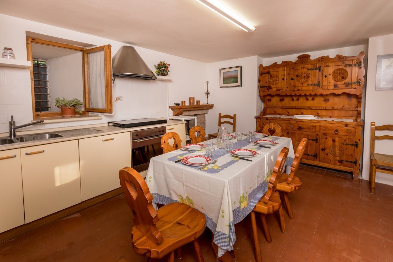 A kitchen with a dining table set for four, wooden cabinets, a stove, and a large wooden cabinet with intricate designs.