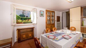 A dining area with a table set for four, wooden chairs, a window with a view of greenery, and a cabinet with glass doors. - Borgo Santa Lucia Apartment with Private Parking & Garden (Gubbio)
