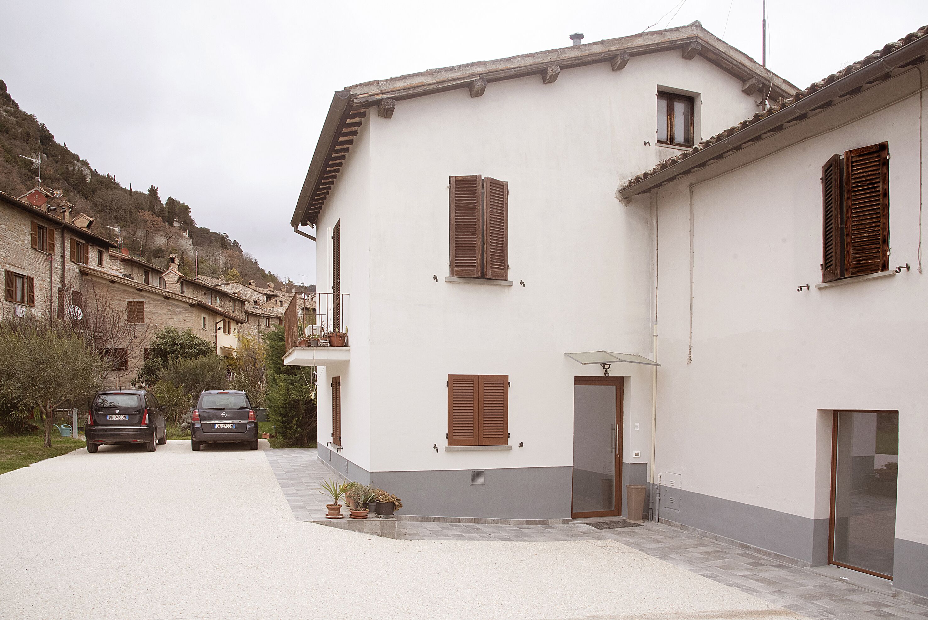 A two-story building with a white facade, wooden shutters, and a small balcony.