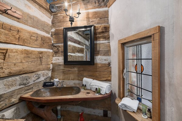 Un baño rústico con un lavabo de madera, un espejo y una ventana de vitral.