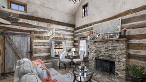 Un interior rústico con vigas de madera a la vista, una chimenea de piedra y un rincón de estar acogedor con sofá y sillones.