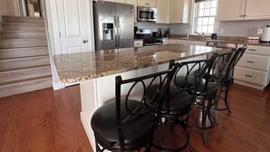 A modern kitchen with white cabinets, stainless steel appliances, a granite countertop, and a bar area with stools. - 4 BR / 2 Bath / Town Center -Top Floor w/ Roofdeck (Ocean City)