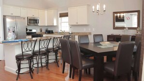 A modern kitchen with white cabinets, stainless steel appliances, and a dining area with dark chairs and a large table. - 4 BR / 2 Bath / Town Center -Top Floor w/ Roofdeck (Ocean City)