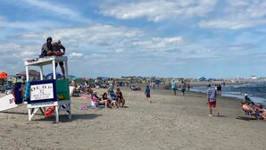 A beach scene with a lifeguard tower labeled "WATCH FOR CHILDREN" and "O.C.B.P. 32 SWIM BETWEEN GREEN FLAGS". - 4 BR / 2 Bath / Town Center -Top Floor w/ Roofdeck (Ocean City)