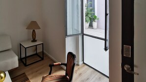 A room with a chair, a small table with a lamp, and a view of the outside through a large window.