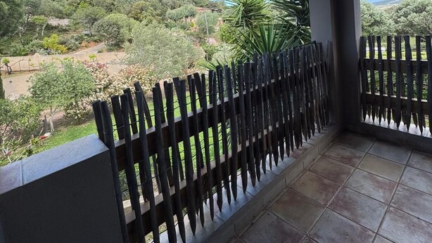 Un espace extérieur abrité offrant une vue sur un jardin aménagé et des collines.