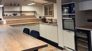 Une cuisine moderne avec une table en bois, des appareils électroménagers intégrés et des luminaires suspendus.