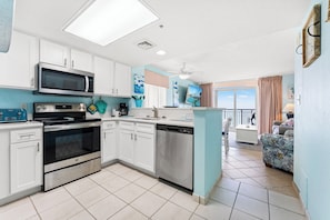 A modern kitchen with white cabinets, stainless steel appliances, and a teal accent wall.