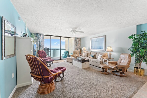 A spacious living room with a large window, a ceiling fan, and a view of the ocean.