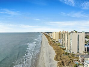 A coastal view with a beachfront hotel, a sandy beach, and ocean waves.