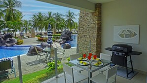 A dining area with a view of a pool and palm trees, a stone wall, and a grill.