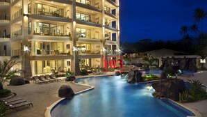 A multi-story hotel with a pool area featuring a waterfall and lounge chairs.