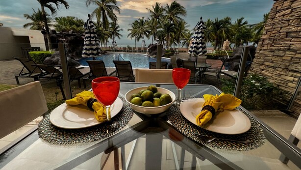 A table set for two with a bowl of fruit, two red glasses, and yellow napkins.