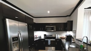 A modern kitchen with stainless steel appliances, black cabinetry, and a black countertop.