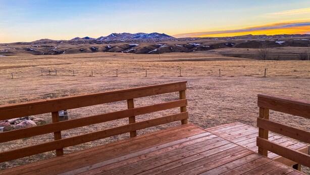 A wooden deck with benches overlooking a mountainous landscape with snow patches. - FOOTHILLS LOOKOUT INN -Come home to Montana! (Havre)