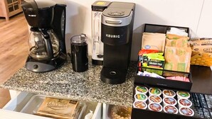 A kitchenette with a coffee maker, a blender, a coffee grinder, and a basket of snacks. - FOOTHILLS LOOKOUT INN -Come home to Montana! (Havre)