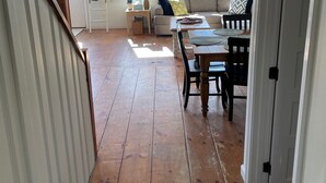 A spacious room with a wooden floor, a dining table with chairs, a sofa, and a window with a view of the outside. - Buoy Beach House Wells (Wells)