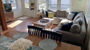 A cozy living room with a wooden dining table, a sofa, and a TV. - Buoy Beach House Wells (Wells)