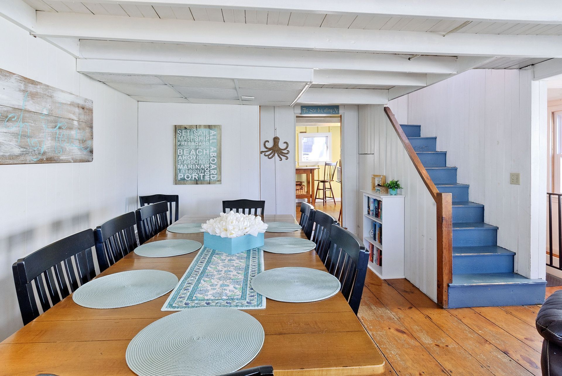 A dining area with a wooden table, black chairs, and a blue centerpiece. There is a staircase with blue steps and a white railing.