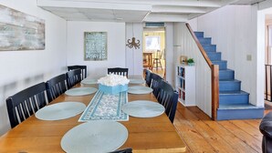 A dining area with a wooden table, black chairs, and a blue centerpiece. There is a staircase with blue steps and a white railing. - Buoy Beach House Wells (Wells)