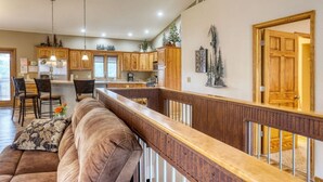 Una cocina espaciosa con armarios de madera, un comedor con sillas y una sala de estar con sofá y barandilla de madera.