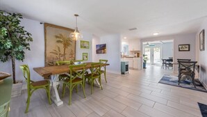 Un vaste espace dédié à la salle à manger, avec une table en bois et des chaises vertes, une grande plante et une vue sur la cuisine.