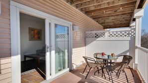 A covered patio with a table and chairs, a sliding glass door, and a white fence. - Deluxe One -Bedroom Condo! (Ocean City)