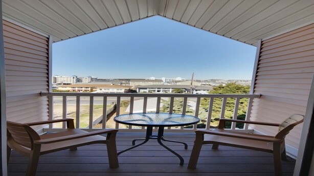 A covered balcony with a table and two chairs, overlooking a residential area with houses and a road. - Deluxe One -Bedroom Condo! (Ocean City)
