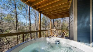A hot tub on a wooden deck with a view of a forest.