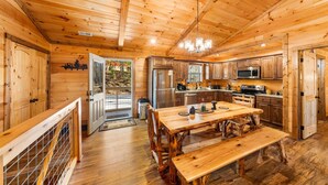 A wooden cabin interior with a kitchen, dining area, and a door leading to a deck.