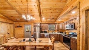 A wooden cabin interior with a dining table, chairs, a refrigerator, a microwave, a stove, and a sink.